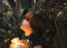 A young child gazes in wonder while holding a jar of lights in a magical forest setting, capturing innocence and curiosity.